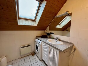 A compact bathroom with a skylight, a washing machine, a sink, and a mirror.