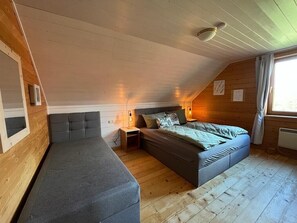 A loft bedroom with a bed, a sofa, wooden walls, a window, and a ceiling light.