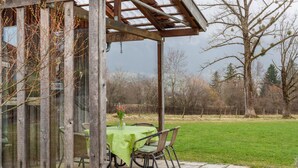 A covered patio with a table and chairs, a glass enclosure, and a view of a grassy field and trees. - Apartment "Mair - Sonnaufgang" with Mountain View, Shared Terrace & Wi-Fi (Halblech)