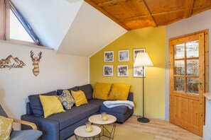 Una sala de estar acogedora con un sofá azul, cojines amarillos, techo de madera y una puerta con paneles de vidrio esmerilado.