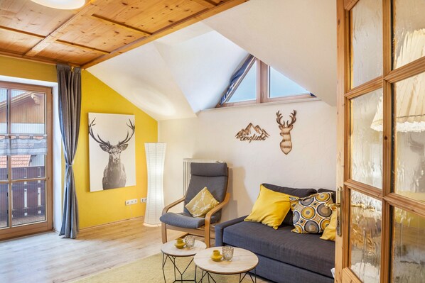 Una habitación acogedora con techo de madera, un sofá con cojines estampados, una silla y una cabeza de venado colgada en la pared.