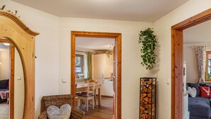 A room with a wicker chair, a dining table with chairs, a mirror, a plant, and a stack of firewood. - Apartment "Mair - Bergblick" with Mountain View, Shared Terrace & Wi-Fi (Halblech)