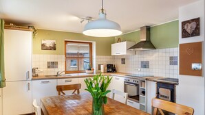 A kitchen with white cabinets, a wooden table, a hanging light fixture, and a window with blinds. - Apartment "Mair - Bergblick" with Mountain View, Shared Terrace & Wi-Fi (Halblech)