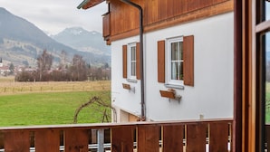 A two-story building with wooden exterior and white walls, featuring a balcony with a wooden railing. - Apartment "Mair - Bergblick" with Mountain View, Shared Terrace & Wi-Fi (Halblech)