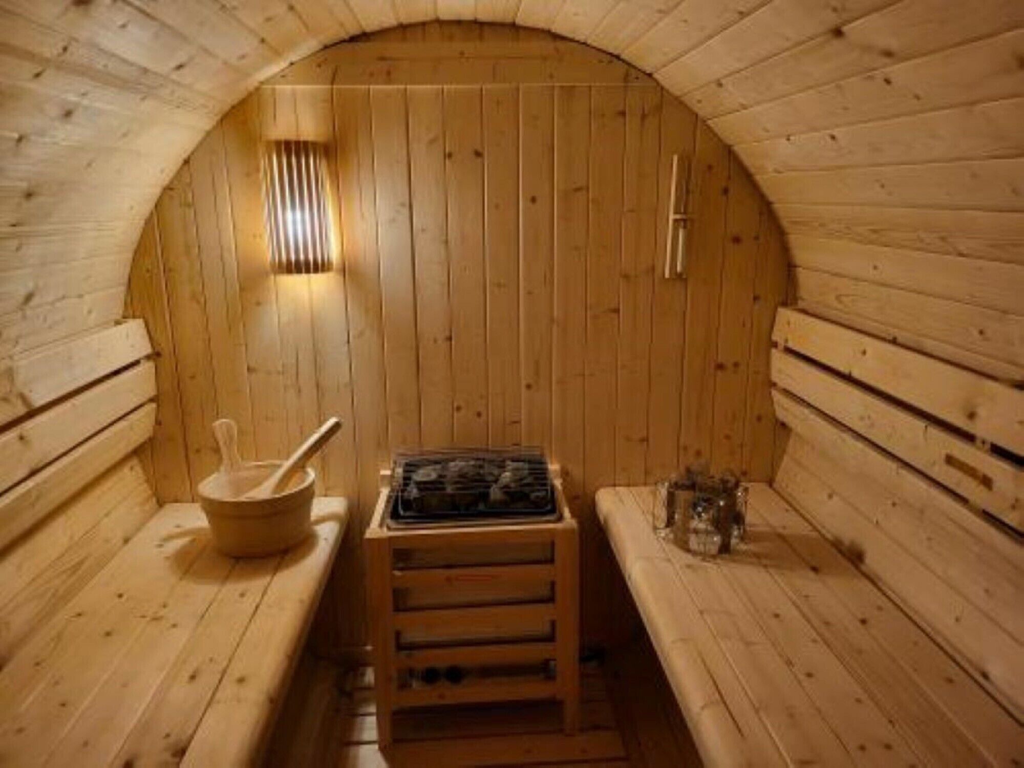 A sauna with wooden walls, benches, a heater, a wooden bowl, and a spoon.