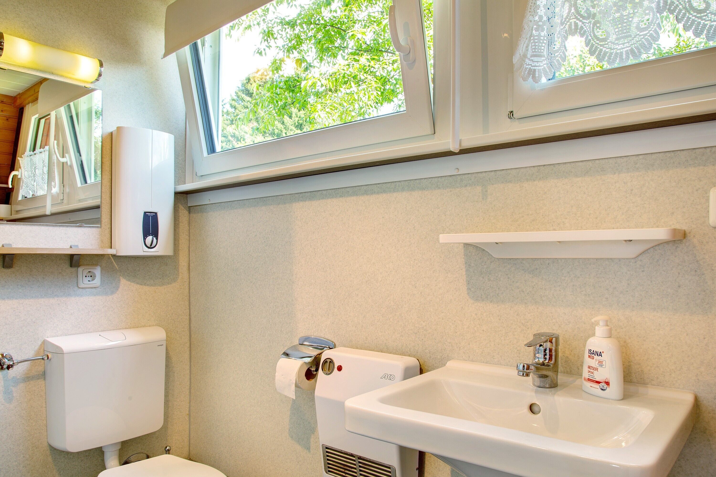 Een badkamer met toilet, wastafel, raam en een fles handdesinfectiemiddel.