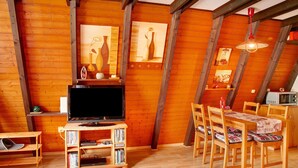 A wooden interior with a television, bookshelves, a dining table with chairs, and a ceiling fan. - Vacation Home "Villa Königsdorf Am See" with Lake View, Private Terrace & Wi-Fi (Waldkirchen)