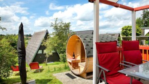 A wooden cylindrical structure with a bench and a table, surrounded by red chairs, under a covered area with a red roof. - Vacation Home "Villa Königsdorf Am See" with Lake View, Private Terrace & Wi-Fi (Waldkirchen)