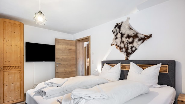 A hotel room with a bed, wooden wardrobe, and a mounted animal head on the wall. - Holiday Apartment "Good Life Top 3" with Mountain View, Private Terrace & Wi-Fi (Saalbach-Hinterglemm)