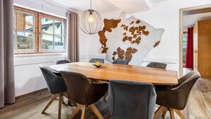 A dining area with a wooden table, six chairs, a pendant light, and a wall-mounted cowhide artwork. - Holiday Apartment "Good Life Top 3" with Mountain View, Private Terrace & Wi-Fi (Saalbach-Hinterglemm)