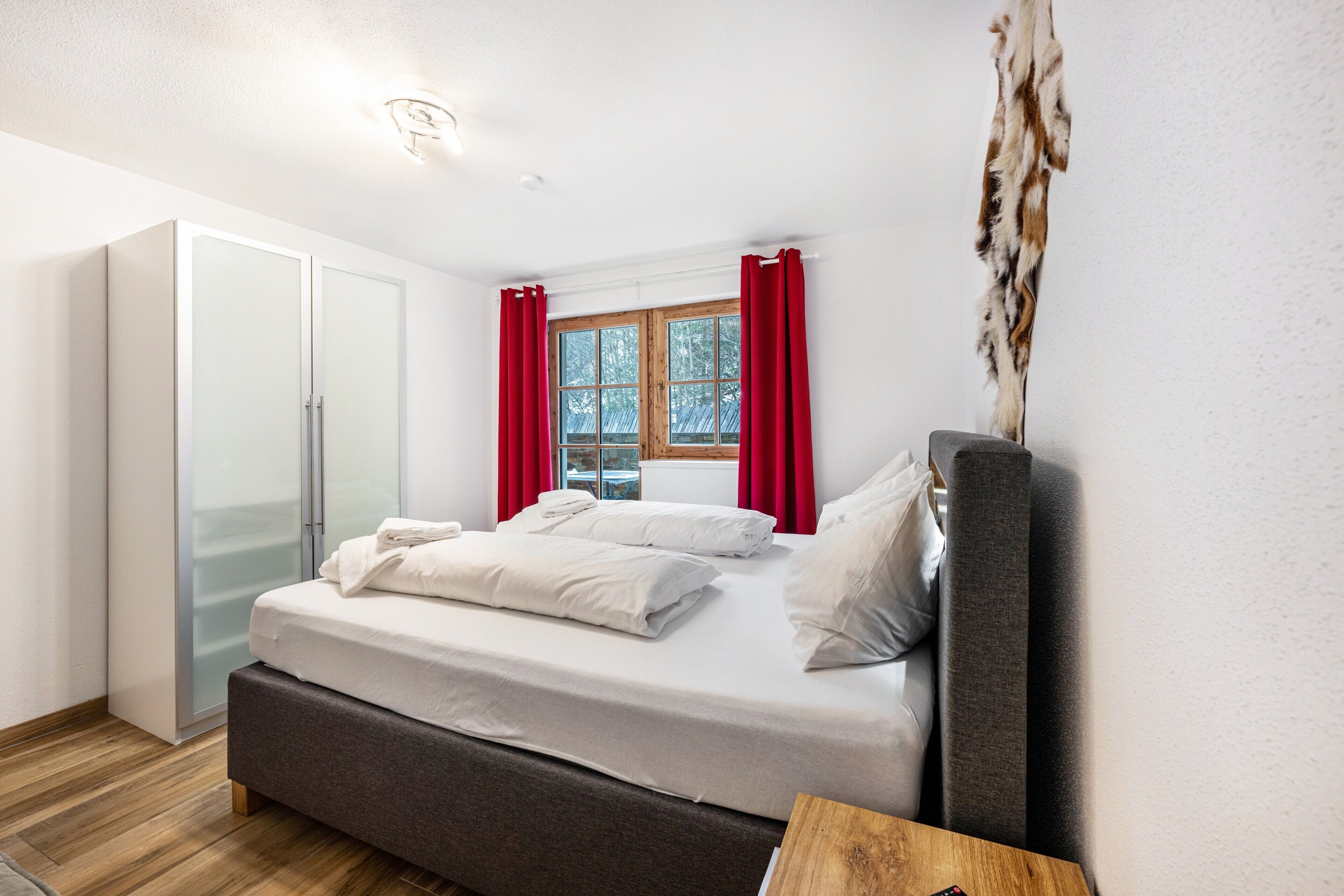 A bedroom with a bed, a wardrobe, a window with curtains, and a wall-mounted artwork.