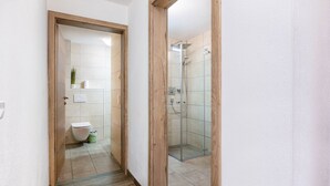 A bathroom with a toilet, a shower, and a mirror. - Holiday Apartment "Good Life Top 3" with Mountain View, Private Terrace & Wi-Fi (Saalbach-Hinterglemm)