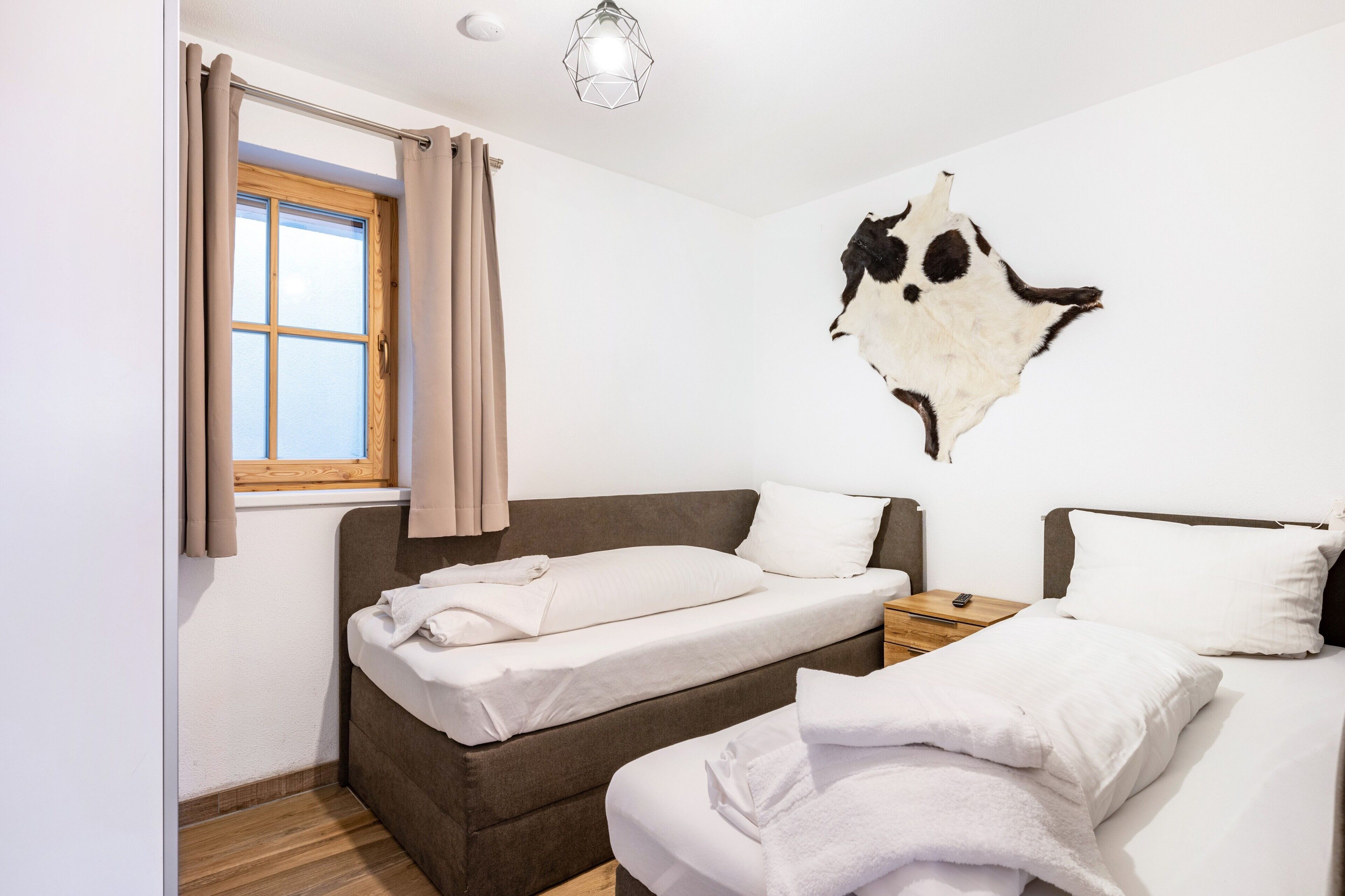Une chambre avec deux lits, une fenêtre avec des rideaux, une table de chevet en bois et un luminaire fixé au mur.