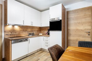 Cocina compacta con armarios blancos, encimera de madera, lavavajillas integrado y refrigerador negro.
