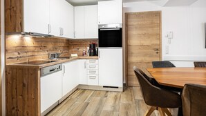A modern kitchen with white cabinets, a built-in oven, and a wooden dining table with chairs. - Holiday Apartment "Good Life Top 3" with Mountain View, Private Terrace & Wi-Fi (Saalbach-Hinterglemm)