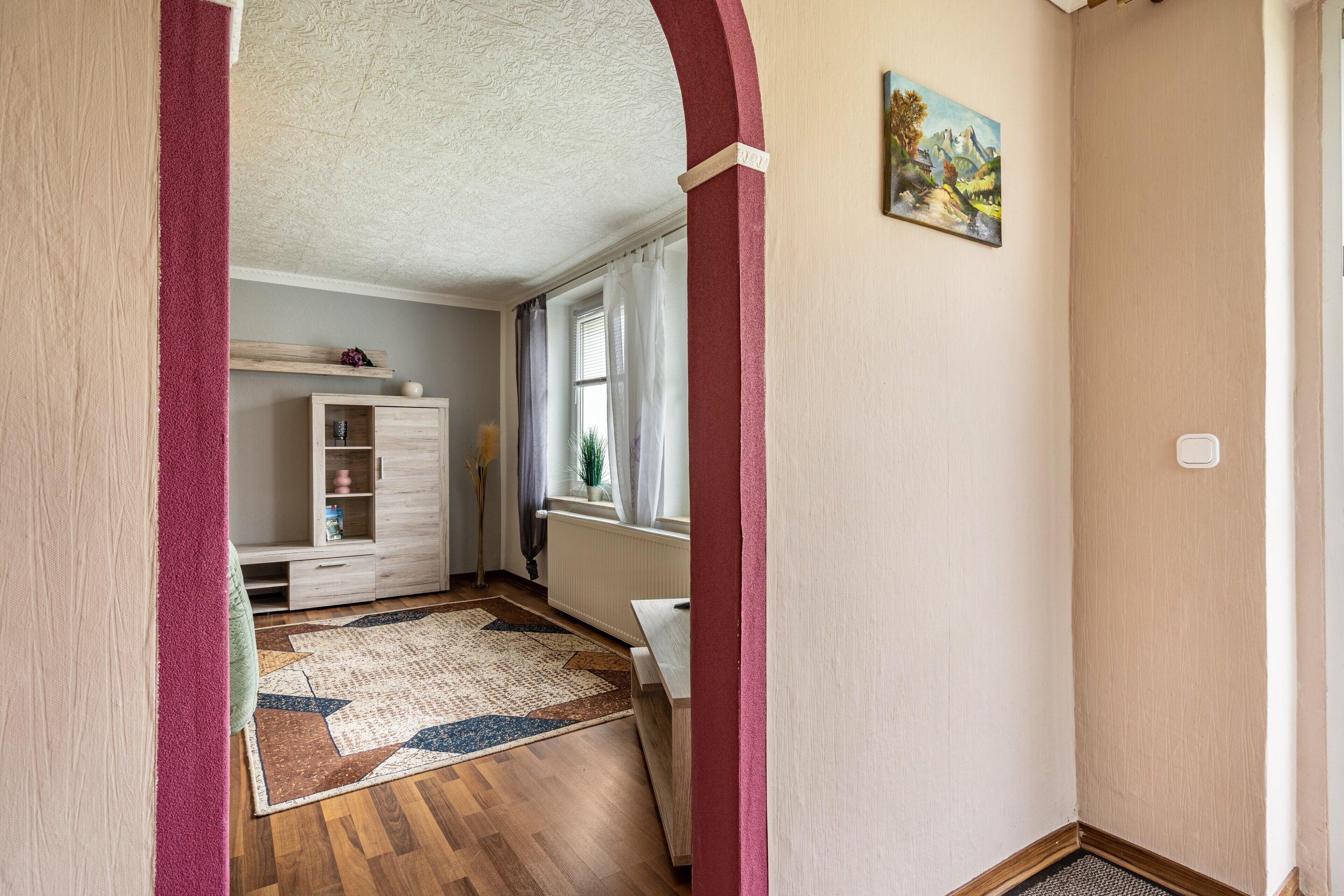 Un corridoio con pavimento in legno, un tappeto decorato, un armadietto bianco, un termosifone e un quadro appeso al muro.