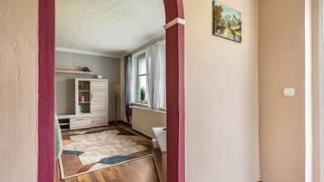 Un corridoio con pavimento in legno, un tappeto decorato, un armadietto bianco, un termosifone e un quadro appeso al muro.