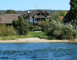 Ein Haus am Seeufer mit Balkon, umgeben von viel Grün und freiem Blick auf den See.