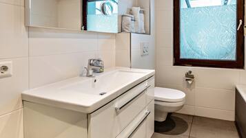 A modern bathroom with a white sink, a toilet, and a window with frosted glass.