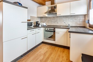 Une cuisine moderne avec des armoires blanches, une cuisinière en acier inoxydable et un plancher en bois.