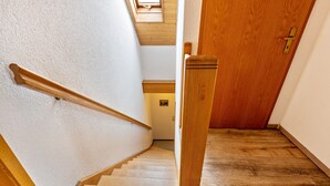 Una escalera de madera con barandilla que conduce a un cuarto con puerta de madera y vistas a un pasillo.