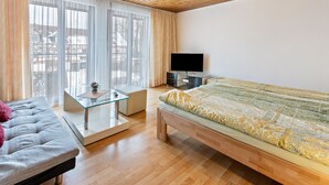 Un dormitorio moderno con cama, sofá, televisor y mesa de vidrio.
