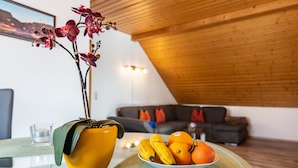 A modern living room with a wooden ceiling, a sofa, a table with a fruit bowl, and a vase with flowers. - Apartment 'Anca' with Lake View, Balcony and Wi-Fi (Öhningen)