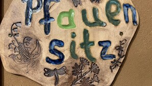 Une plaque de pierre portant l’inscription « Pfauen sitz » et ornée d’éléments décoratifs tels que des fleurs et des papillons.