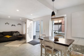 A living room with a sofa, a dining table with chairs, a hanging light fixture, and a door leading to another room. - Studio Holiday Apartment "Lilly" with Wi-Fi (Messkirch)