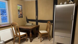 Una habitación con una mesa de madera, dos sillas, un refrigerador, un radiador y una ventana con vistas.