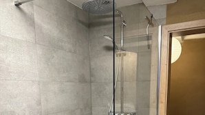 Una ducha con cerramiento de vidrio, cabezal de ducha de mano y grifo empotrado.