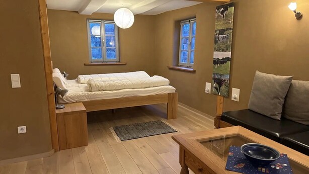 Un dormitorio con cama, sofá, una mesa con un cuenco y un cuadro de vaca en la pared.