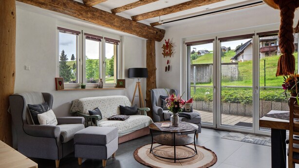 A living room with a sofa, armchairs, a coffee table, and a view through large glass doors to an outdoor area.