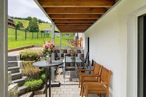 Un patio abrité avec une table, des chaises et un petit coin jardin.