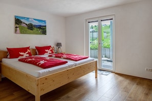 Une chambre à coucher avec un lit en bois, des oreillers rouges, un tableau représentant un paysage et une porte-fenêtre coulissante donnant sur un balcon.