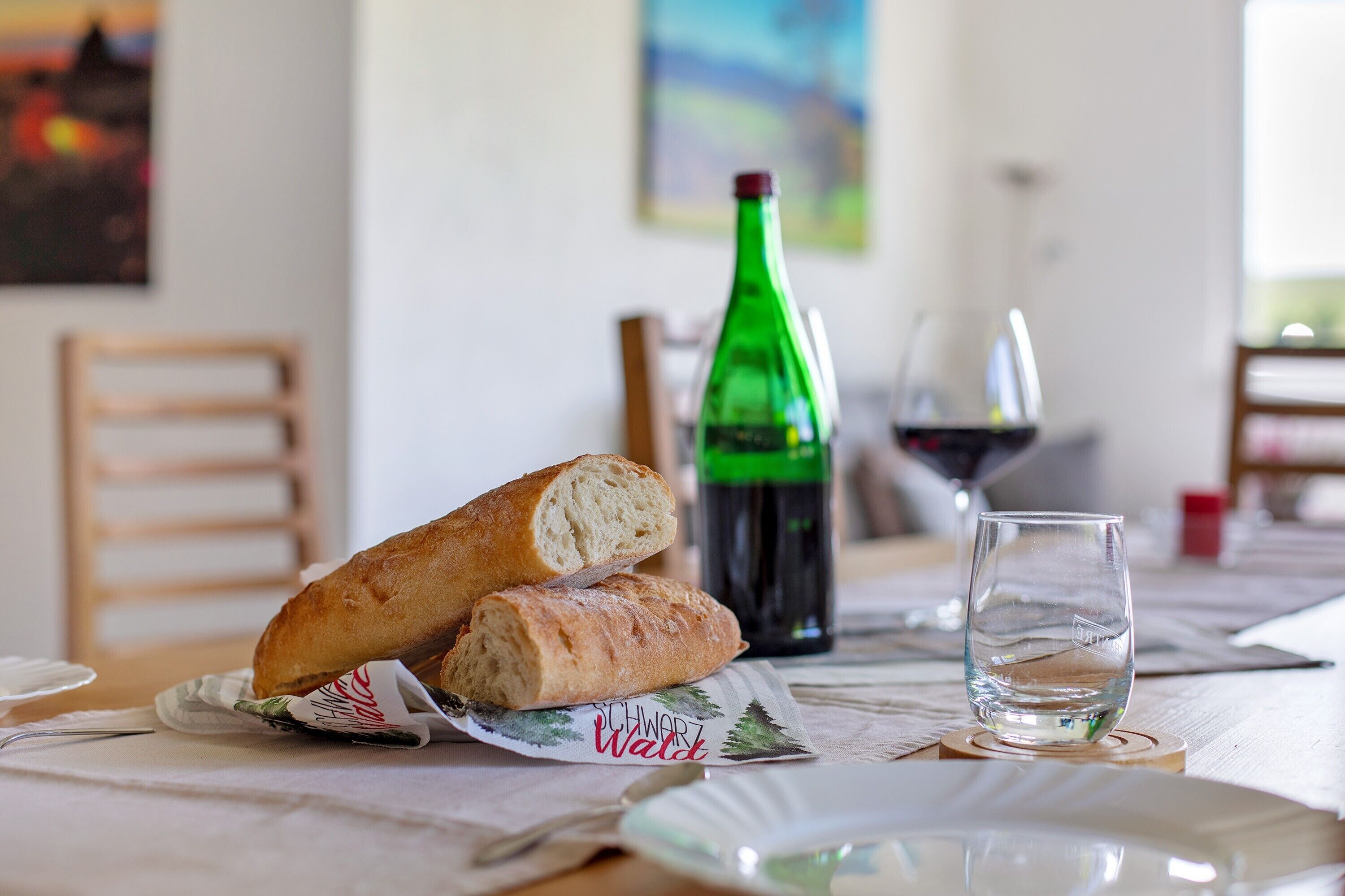 A table with two baguettes, a bottle of wine, and a glass.