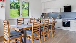 A modern kitchen with white cabinets, a built-in oven, and a dining area with wooden chairs and a table. - Apartment 'Ulrich' with Mountain View, Shared Terrace and Wi-Fi (Oberried-Hofsgrund)
