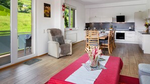 A modern kitchen with a dining area, a sofa, and a view of a green landscape through large windows. - Apartment 'Ulrich' with Mountain View, Shared Terrace and Wi-Fi (Oberried-Hofsgrund)
