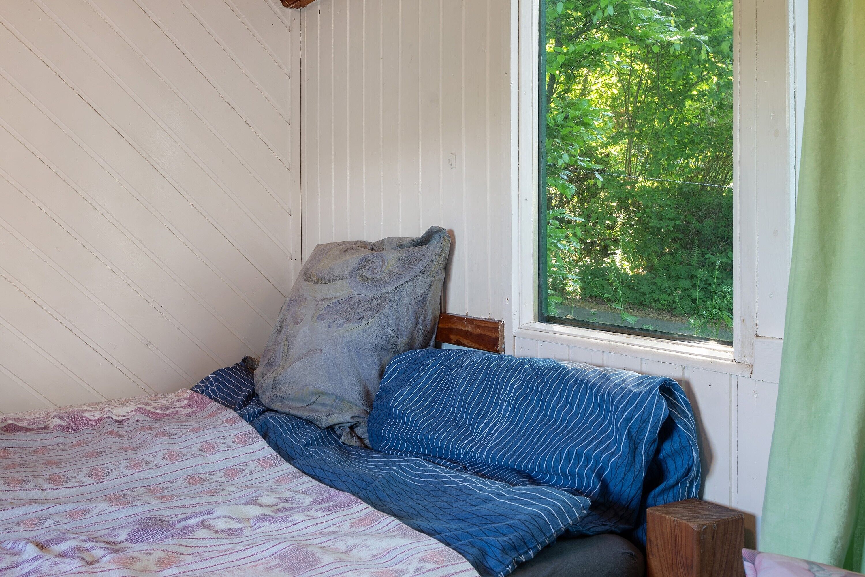 A bedroom with a bed, pillows, a window with a view of greenery, and a wooden nightstand.