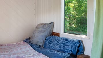 A bedroom with a bed, pillows, a window with a view of greenery, and a wooden nightstand.