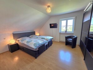 A bedroom with a bed, bedside lamps, a TV, a window, and a small chair.