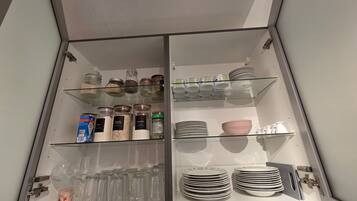 Un armario de cocina con repisas de vidrio que contiene frascos, platos y utensilios.