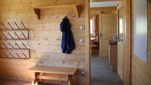 A wooden cabin interior with a bench, coat hooks, and a view into the kitchen area.