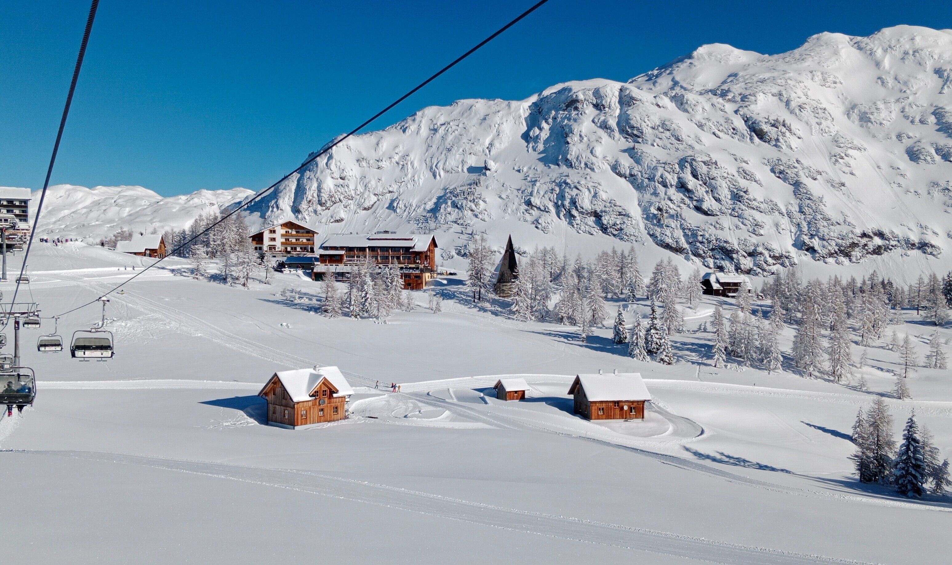 A snow-covered mountain with wooden cabins and a ski lift.
