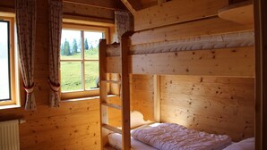 A wooden cabin room with a bunk bed, a window with curtains, and a view of the outdoors.