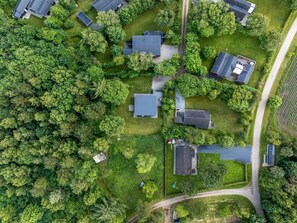 An aerial view of a residential area with multiple houses, surrounded by dense greenery and a clear road.