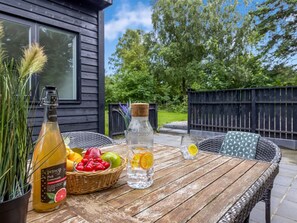 A wooden table with a bottle of pink lemonade, a glass of water, and a basket of fruits.