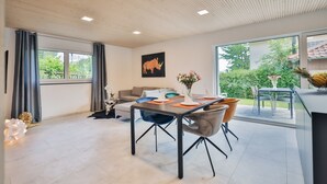 A modern living room with a dining area, large windows, and a painting of a rhinoceros.
