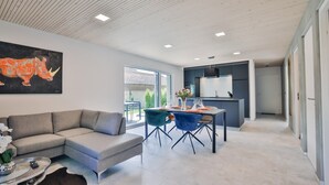 A modern living room with a sofa, dining table, chairs, and a kitchen area.