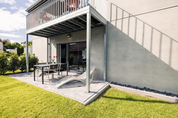 A modern house with a covered patio, a dining area, and a view of the surrounding greenery.